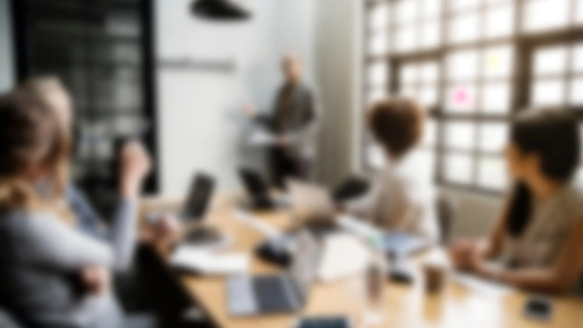Eine Person erklärt am Whiteboard, das Team sitzt mit Laptops am Tisch, unscharf